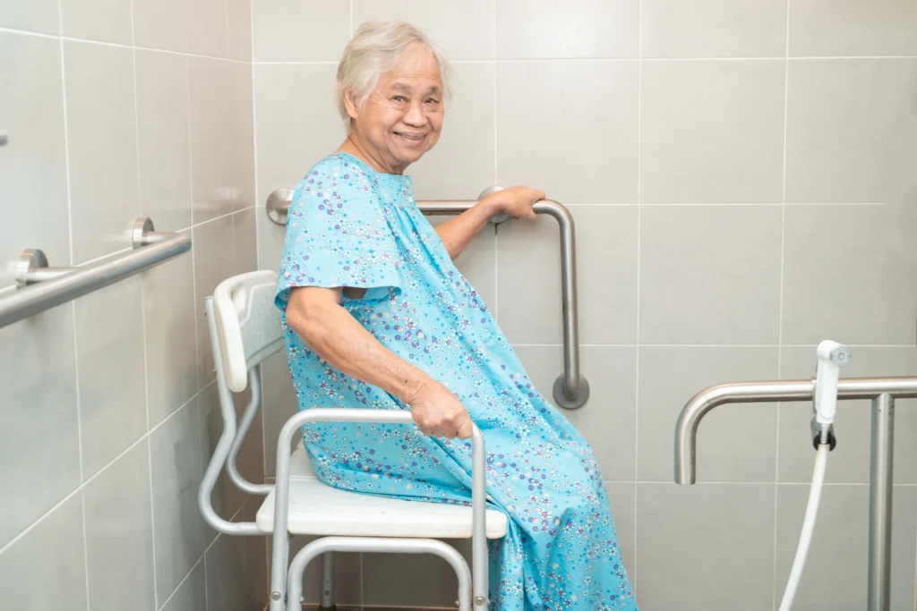 Vista completa de un baño en donde hay una mujer sobre una silla de ducha.