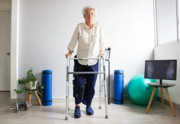 Una mujer usando una andadera como uno de los aparatos para adultos mayores de uso como rehabilitación.