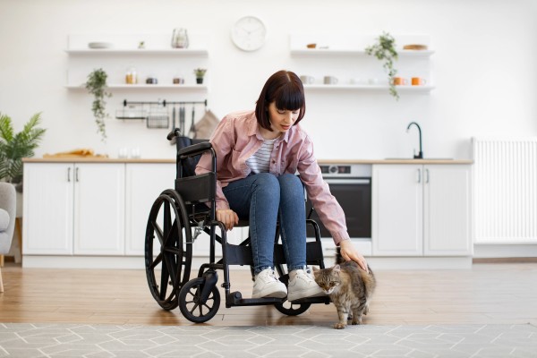 Mujer acariciando a su gato dentro de su departamento gracias a los beneficios de usar una silla de ruedas.