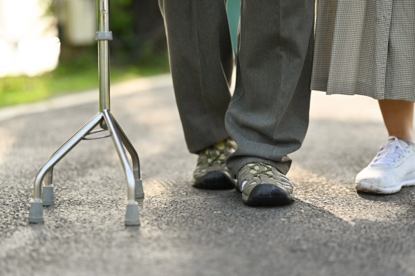 Enfoque en los zapatos de una persona que va usando un bastón que es un aparato ortopédico.